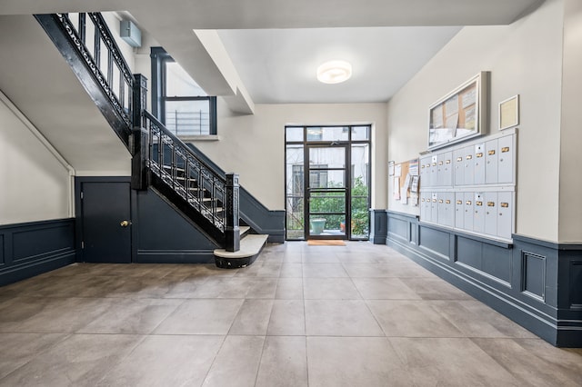 entrance foyer with a decorative wall, mail area, a wainscoted wall, and stairway