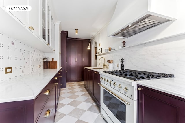 kitchen with sink, high end stove, custom range hood, light stone countertops, and decorative backsplash