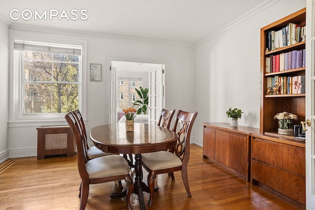 dining room featuring ornamental molding, light wood finished floors, baseboards, and radiator