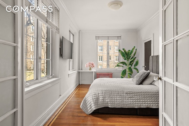 bedroom with ornamental molding and wood finished floors