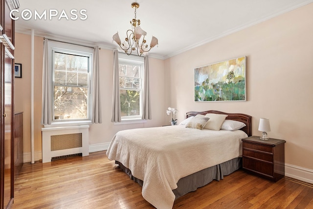 bedroom with baseboards, ornamental molding, radiator, light wood finished floors, and an inviting chandelier