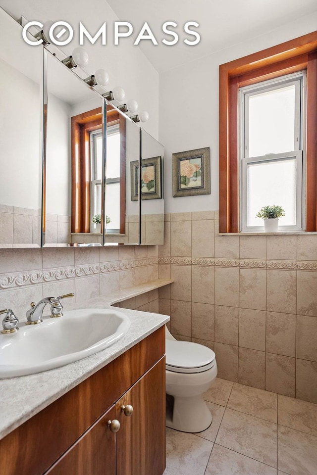 bathroom with a wainscoted wall, tile walls, toilet, vanity, and tile patterned floors