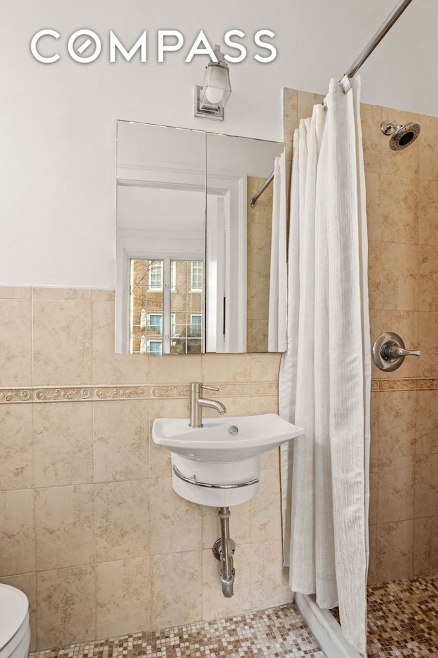 full bath featuring a stall shower, a sink, toilet, and tile walls