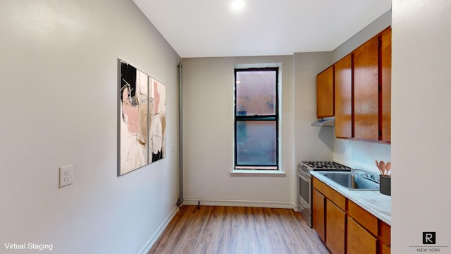kitchen with stainless steel range with gas stovetop, light countertops, a sink, light wood-type flooring, and under cabinet range hood