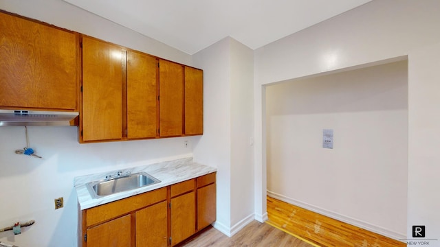 kitchen featuring a sink, light wood-style flooring, light countertops, brown cabinets, and under cabinet range hood