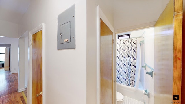 bathroom featuring electric panel, wood finished floors, shower / bath combo, and toilet