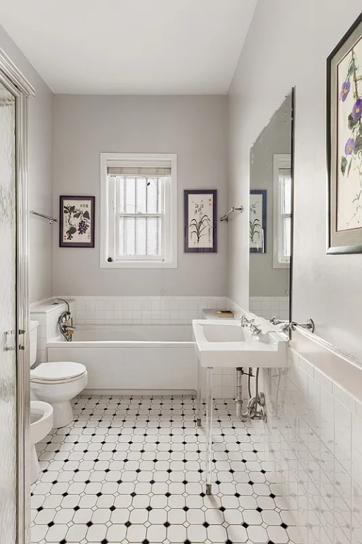 bathroom with a washtub, sink, toilet, tile walls, and a bidet