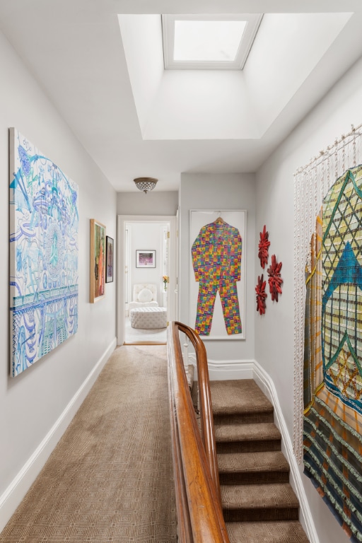 corridor featuring a skylight, a tray ceiling, and carpet floors