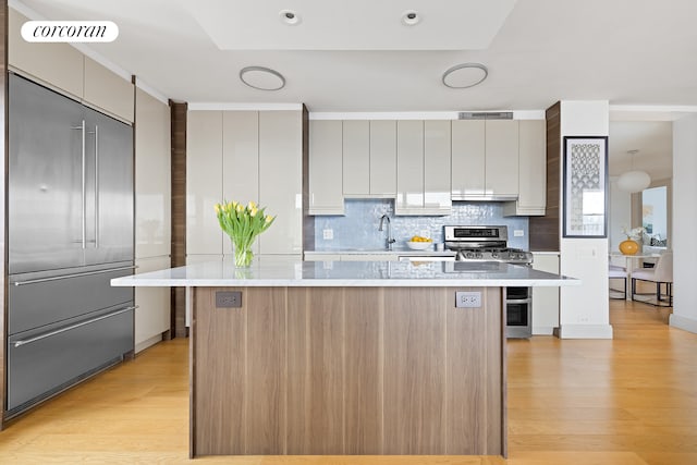 kitchen featuring stainless steel appliances, light countertops, decorative backsplash, a center island, and light wood-style floors