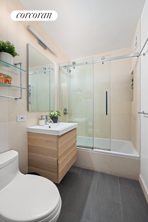 full bathroom with toilet, bath / shower combo with glass door, tile walls, vanity, and tile patterned flooring