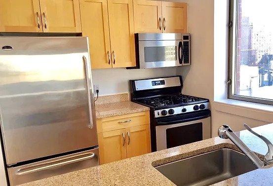 kitchen with a sink, light brown cabinets, light stone countertops, and stainless steel appliances