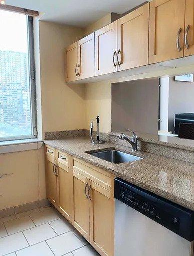 kitchen featuring stainless steel dishwasher, light stone countertops, a sink, baseboards, and light tile patterned flooring