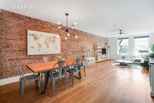 dining area with ceiling fan with notable chandelier, baseboards, brick wall, and wood finished floors