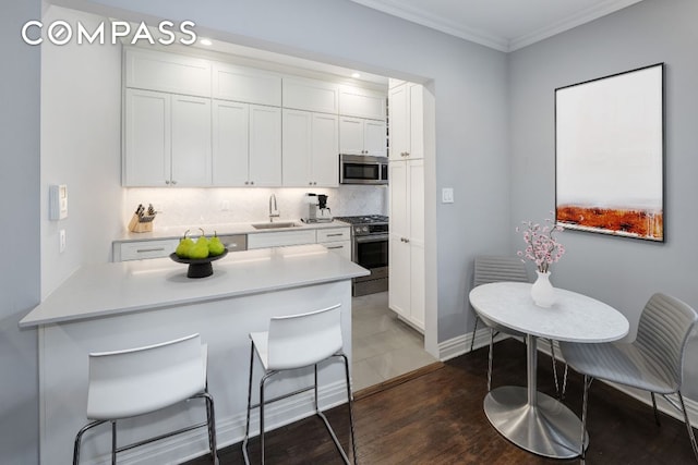 kitchen with decorative backsplash, ornamental molding, stainless steel appliances, light countertops, and white cabinetry