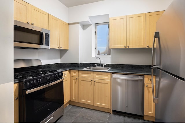 kitchen with dark countertops, light brown cabinets, stainless steel appliances, and a sink