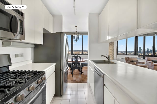 kitchen with pendant lighting, stainless steel appliances, light countertops, white cabinetry, and a sink