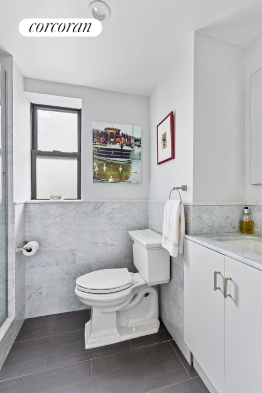 bathroom featuring vanity, toilet, a shower with shower door, and tile walls