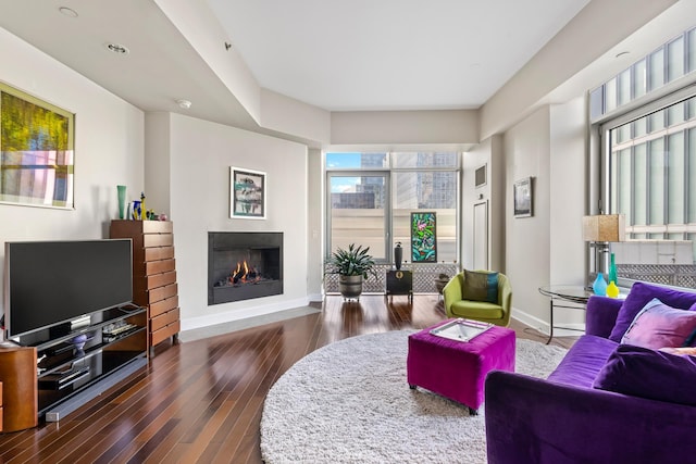 living area featuring baseboards, a warm lit fireplace, and dark wood-style flooring