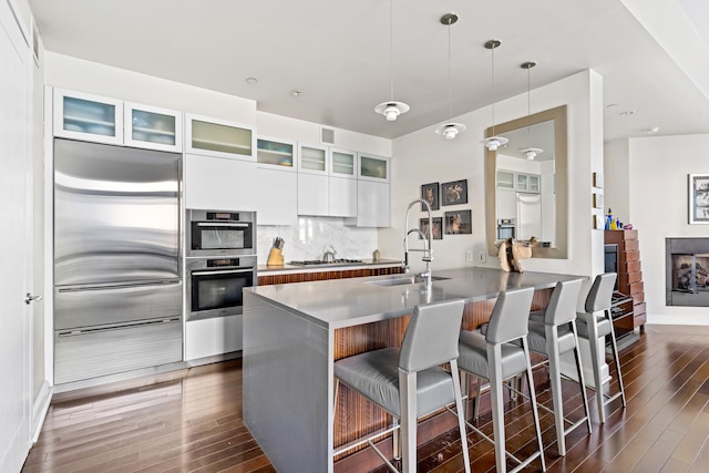 kitchen with modern cabinets, a kitchen bar, dark wood-style flooring, appliances with stainless steel finishes, and white cabinetry