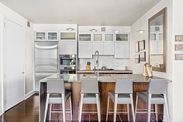 kitchen with appliances with stainless steel finishes, decorative backsplash, a breakfast bar area, and glass insert cabinets