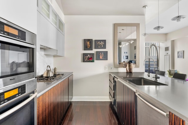kitchen featuring appliances with stainless steel finishes, a sink, modern cabinets, baseboards, and dark wood-style flooring