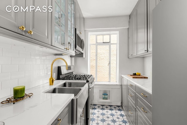 kitchen featuring a wealth of natural light, appliances with stainless steel finishes, glass insert cabinets, and gray cabinetry