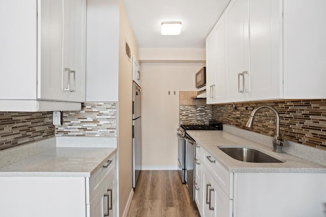 kitchen featuring white cabinets, appliances with stainless steel finishes, light stone countertops, light wood-style floors, and a sink