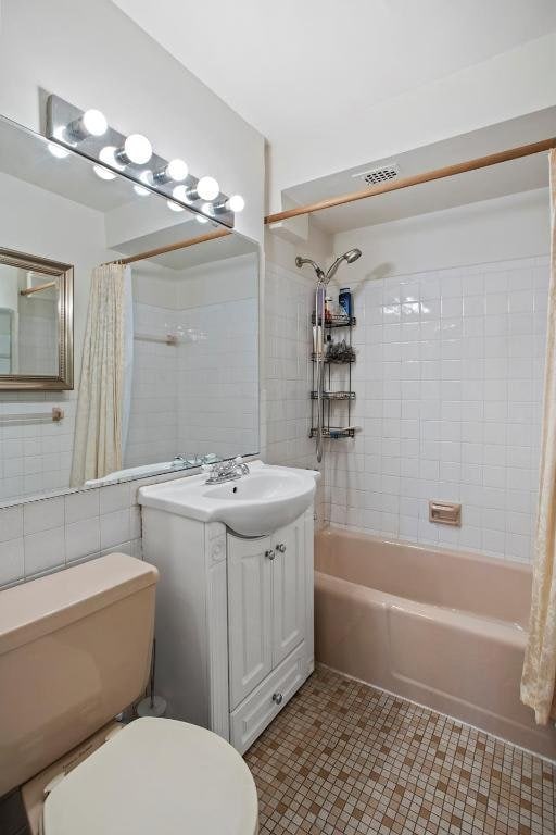 full bathroom with tile walls, toilet, shower / bath combo with shower curtain, vanity, and tile patterned flooring