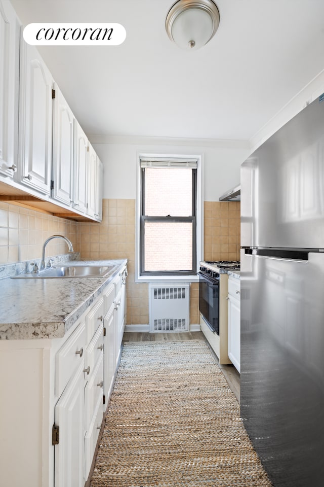 kitchen featuring crown molding, radiator heating unit, freestanding refrigerator, white cabinetry, and gas range