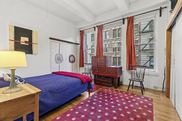 bedroom with beamed ceiling, wood-type flooring, and a closet