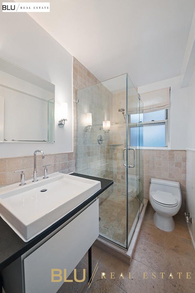 full bath with vanity, toilet, tile walls, a wainscoted wall, and a stall shower