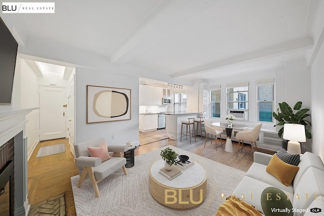 living area with beamed ceiling, a fireplace with flush hearth, and light wood-style floors