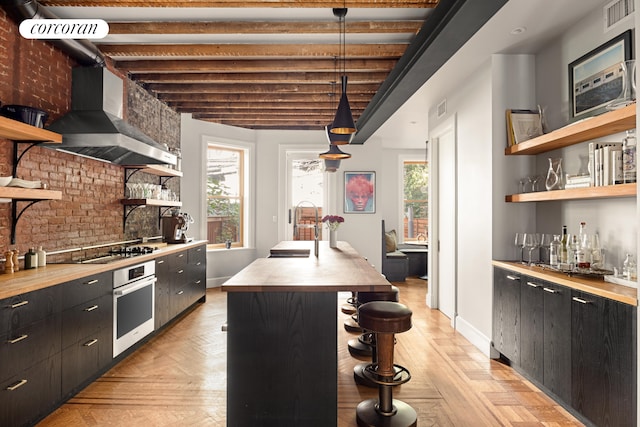 kitchen with open shelves, a sink, appliances with stainless steel finishes, wall chimney exhaust hood, and butcher block counters