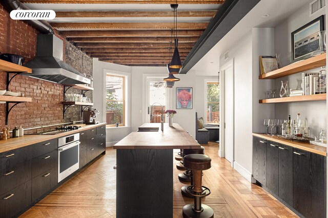 kitchen with open shelves, a sink, appliances with stainless steel finishes, wall chimney exhaust hood, and butcher block counters