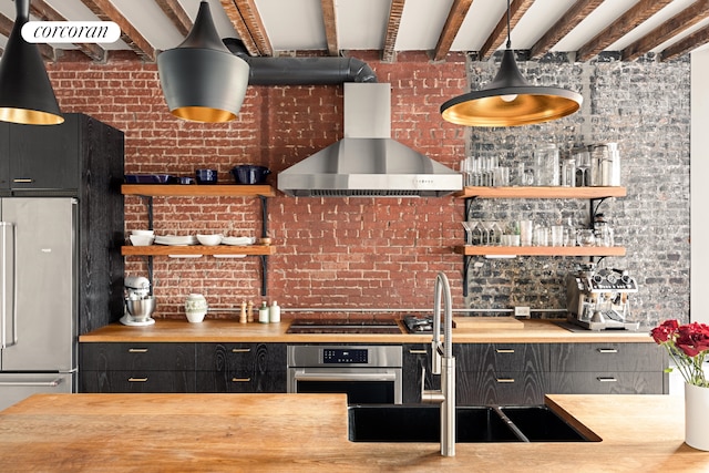 kitchen with built in fridge, a sink, stainless steel oven, wood counters, and wall chimney exhaust hood