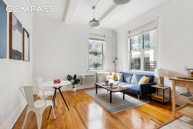 living area with radiator, hardwood / wood-style floors, an AC wall unit, beamed ceiling, and baseboards