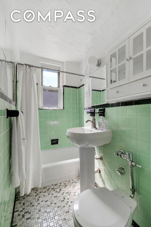 full bathroom with a textured ceiling, toilet, tile walls, and shower / bathtub combination with curtain