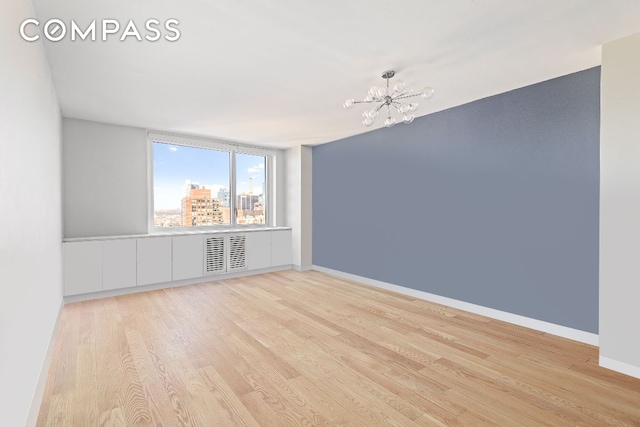 unfurnished room with a view of city, a notable chandelier, visible vents, light wood-style flooring, and baseboards