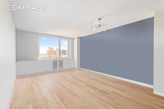 spare room featuring wood finished floors, a chandelier, baseboards, and a view of city