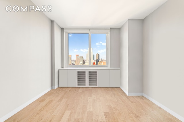 unfurnished room with light wood finished floors, baseboards, and a city view