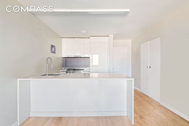 kitchen with white cabinets, light countertops, a sink, and light wood-style floors