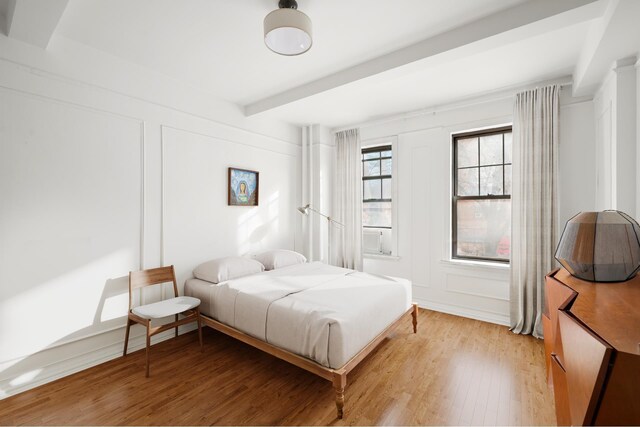 bedroom with light wood finished floors, a decorative wall, and beam ceiling