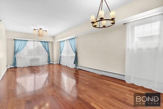 empty room featuring a healthy amount of sunlight, a baseboard radiator, an inviting chandelier, and wood finished floors