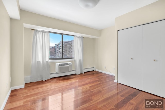 unfurnished bedroom with an AC wall unit, baseboards, and wood finished floors