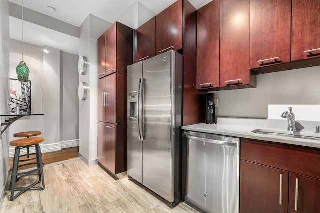 kitchen with light wood finished floors, dark brown cabinets, light countertops, stainless steel appliances, and a sink