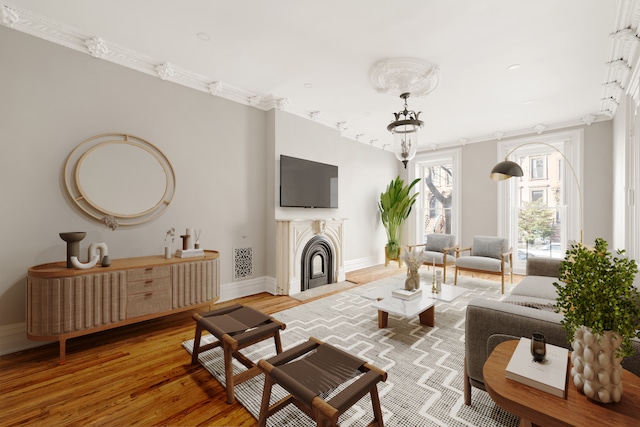 living room with light wood finished floors, a notable chandelier, crown molding, a fireplace, and baseboards