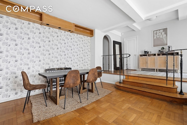 dining space featuring arched walkways, beamed ceiling, and baseboards