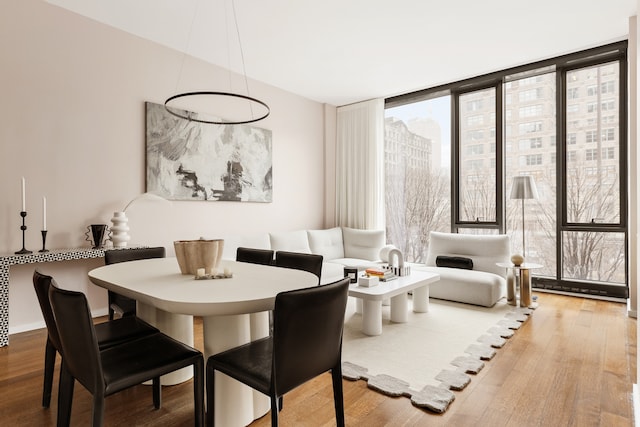 dining room featuring a wall of windows, baseboards, wood finished floors, and a view of city