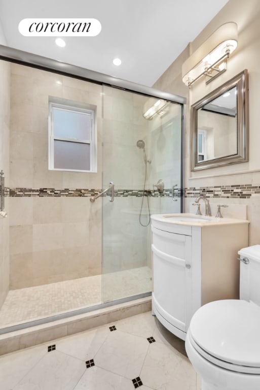 bathroom featuring tile walls, vanity, toilet, and a shower with shower door