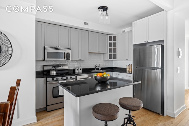 kitchen with appliances with stainless steel finishes, light wood-style floors, a sink, and tasteful backsplash